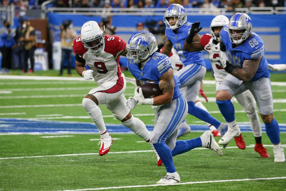 American football player runs with the ball while being pursued by two players of the opposite team