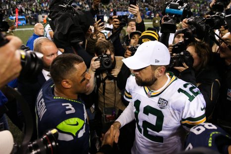 American football players shake hands while surrounded by the media after a game