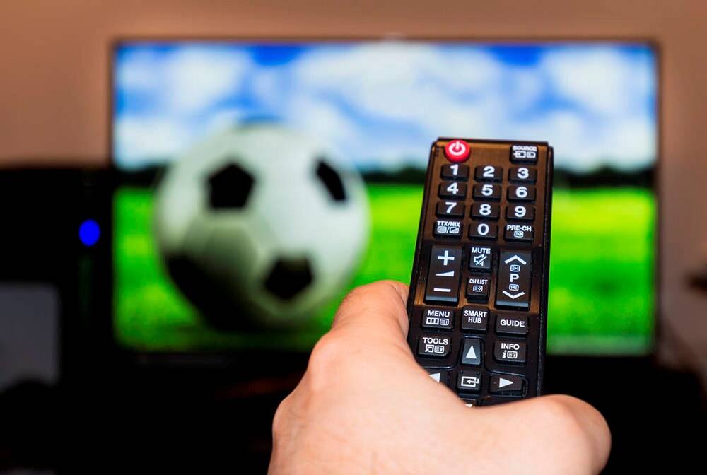 Watching football game on modern tv, with a close-up of the remote control